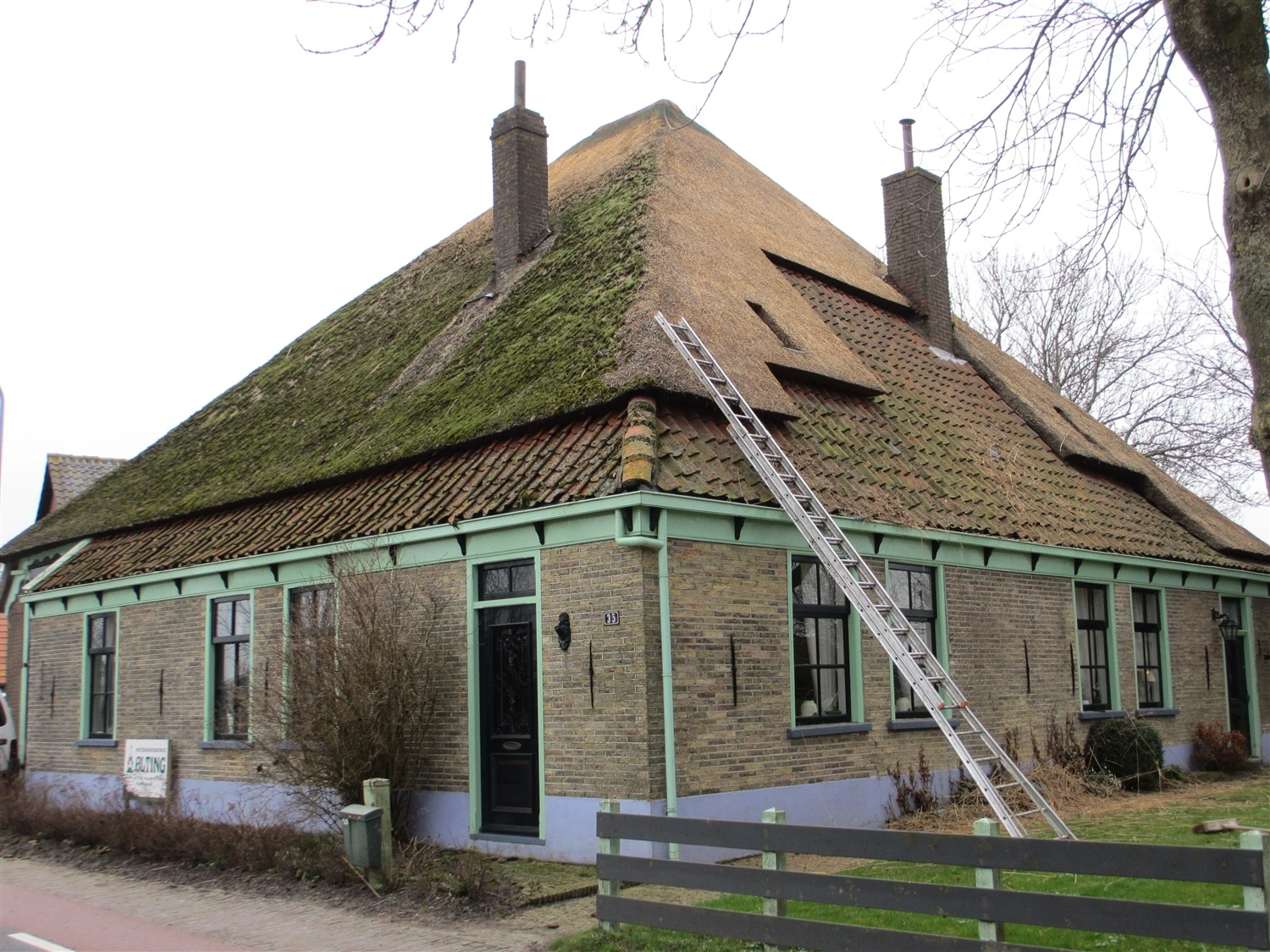 Boerderij in Noord-Holland tijdens rieten dak renovatie door Alting Rietbeheer, met zichtbare mosgroei op het nog te vernieuwen deel